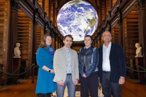 Four people standing in a library in front of an image of the Earth
