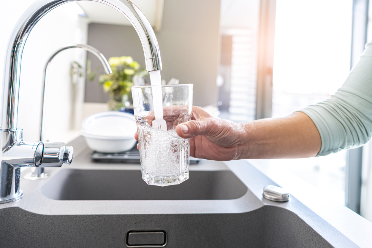 person filling a glass with water from a tap at home