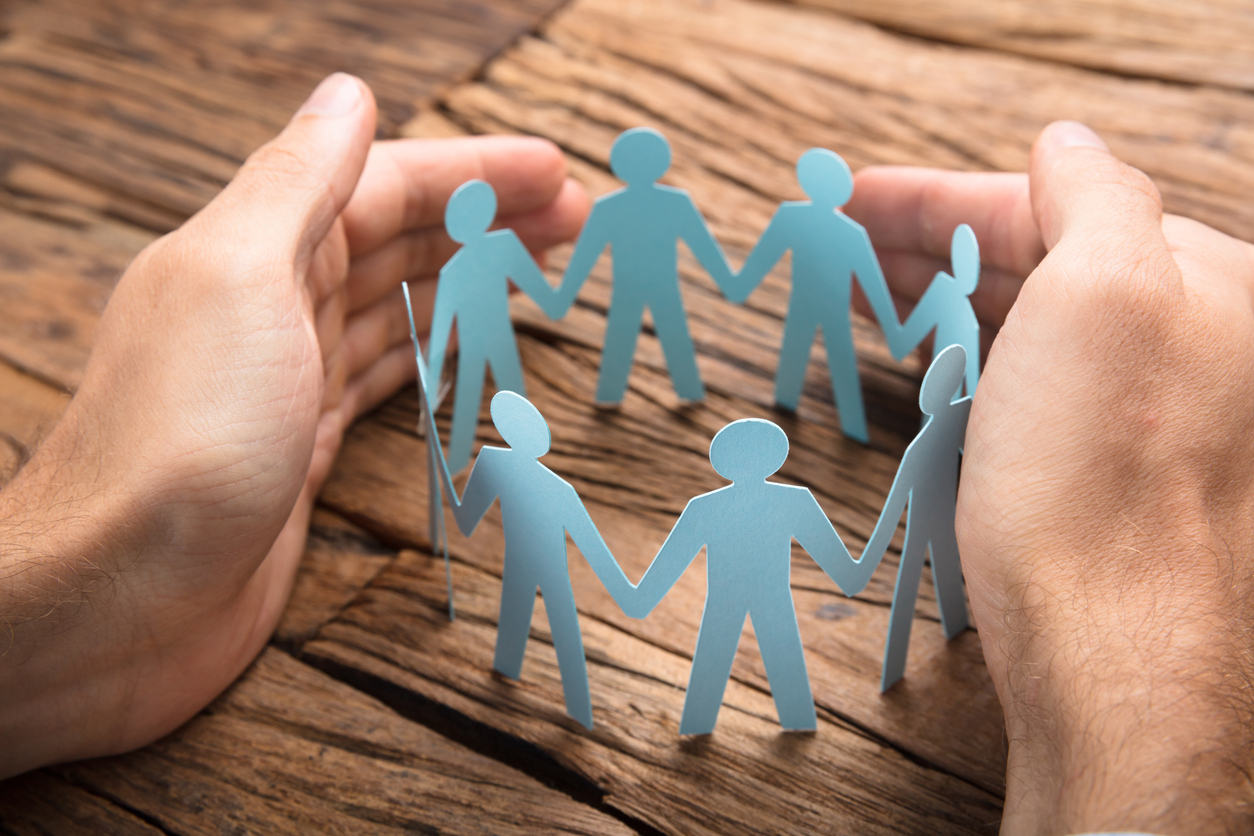 abstract image of hands held around chain of paper stick figures